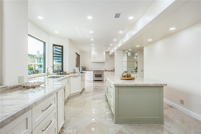 kitchen with light stone countertops, a sink, white cabinetry, visible vents, and a center island