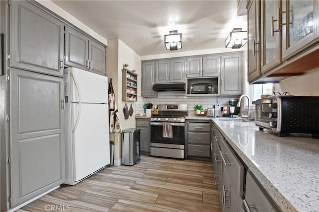 kitchen with stainless steel gas range oven, freestanding refrigerator, gray cabinets, under cabinet range hood, and a sink