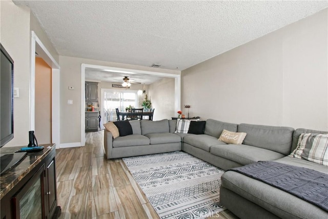 living room with a ceiling fan, visible vents, a textured ceiling, and light wood finished floors