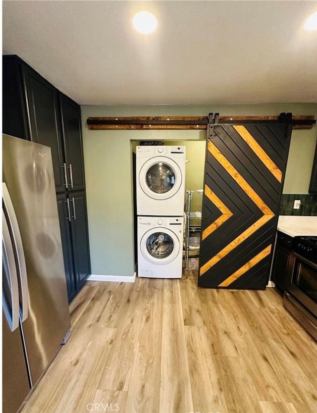 washroom with stacked washer and dryer, a barn door, laundry area, and light wood finished floors