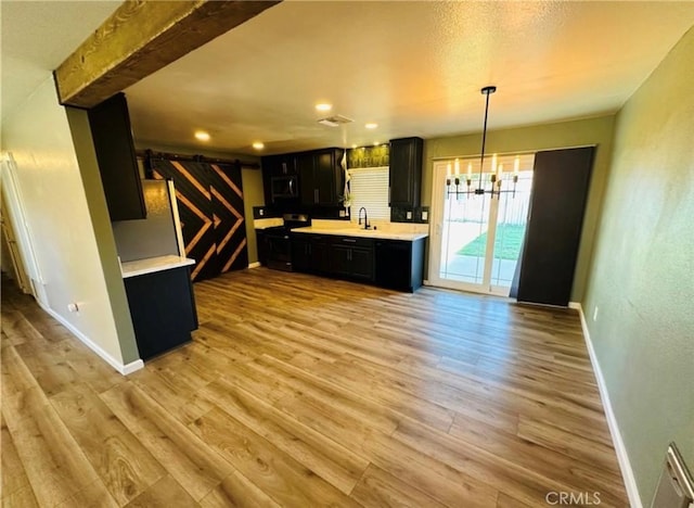 kitchen with light countertops, a barn door, light wood-style floors, a sink, and dark cabinetry