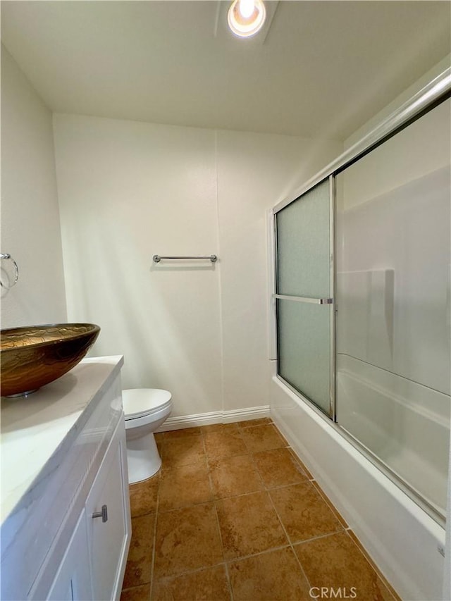 bathroom with baseboards, toilet, shower / bath combination with glass door, tile patterned floors, and vanity