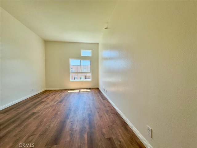 empty room featuring a baseboard heating unit, baseboards, and dark wood finished floors