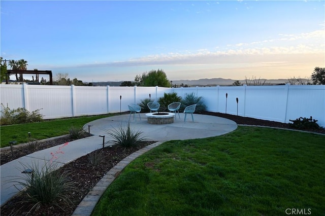 yard at dusk with an outdoor fire pit, a fenced backyard, and a patio