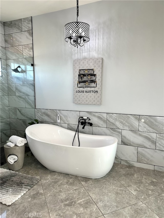 full bathroom with tiled shower, an inviting chandelier, marble finish floor, a freestanding tub, and tile walls