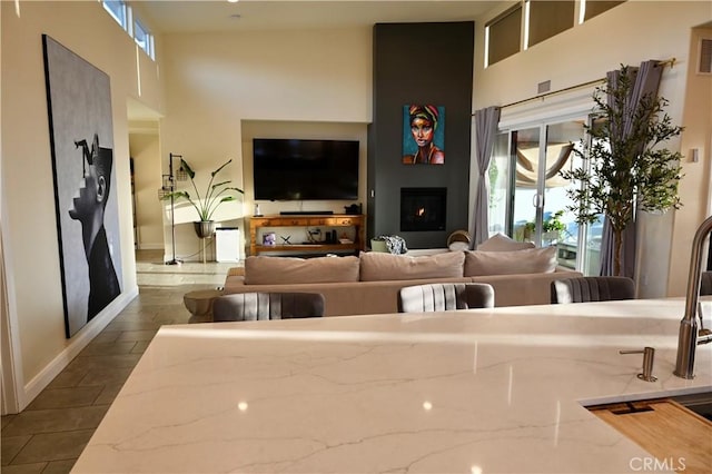 living room featuring a warm lit fireplace, a high ceiling, and plenty of natural light