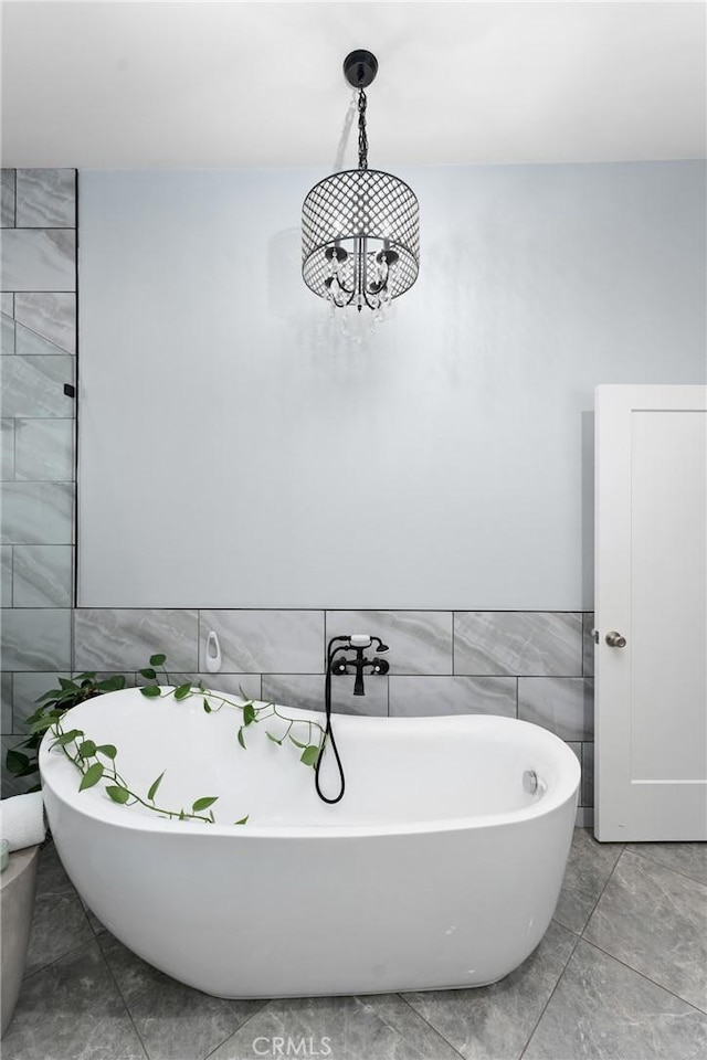 full bath featuring a chandelier, tile walls, marble finish floor, and a freestanding bath