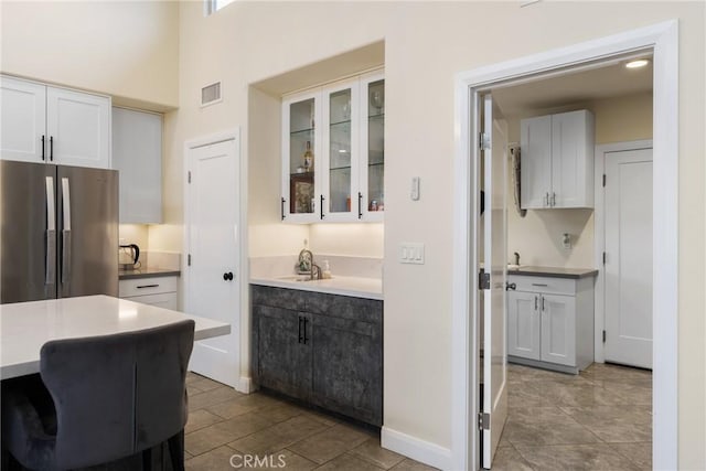 kitchen featuring white cabinets, light countertops, freestanding refrigerator, visible vents, and glass insert cabinets