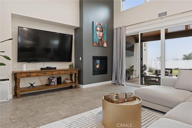 living room with baseboards, a towering ceiling, a glass covered fireplace, and visible vents