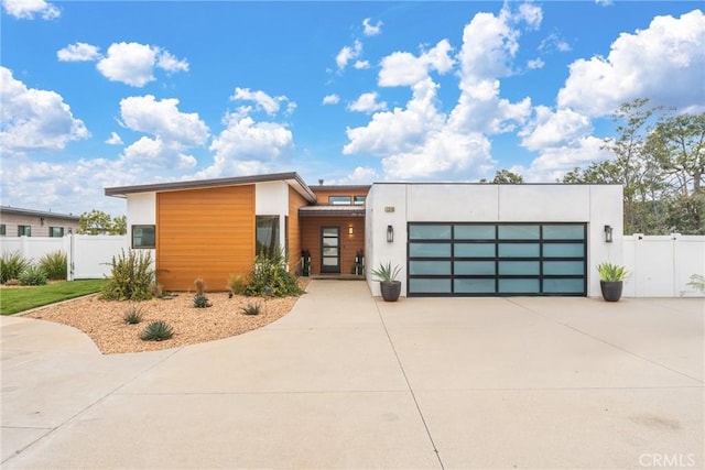 modern home featuring stucco siding, a garage, fence, and driveway