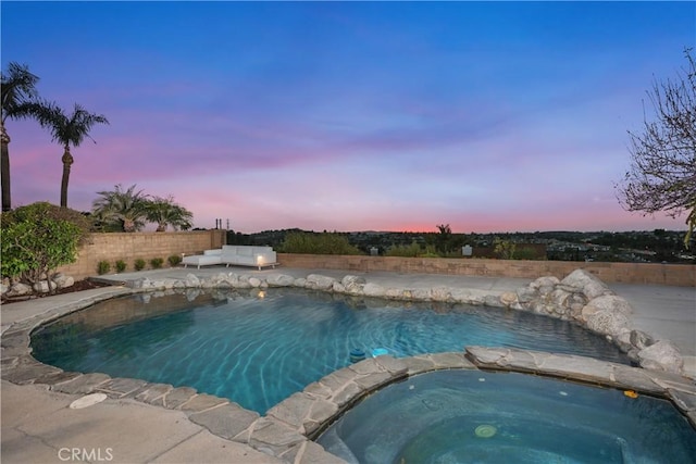 pool at dusk with an in ground hot tub, fence, and an outdoor pool