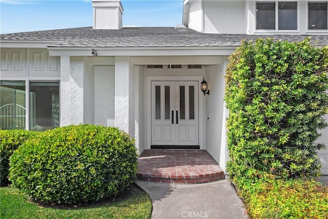 view of exterior entry with a shingled roof and stucco siding