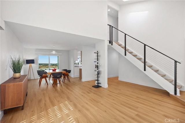 dining area featuring a towering ceiling, light wood-type flooring, stairway, and baseboards