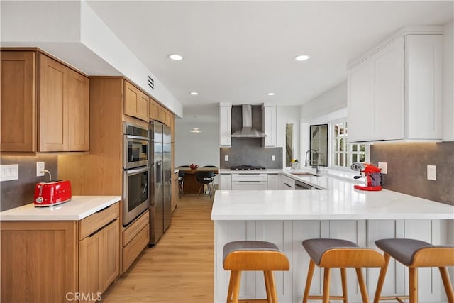 kitchen featuring a breakfast bar area, a sink, a peninsula, and wall chimney exhaust hood