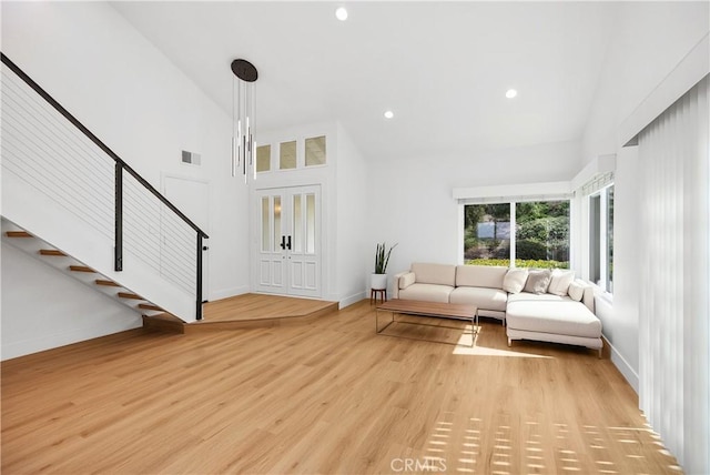 interior space with light wood-style flooring, a high ceiling, visible vents, baseboards, and stairway