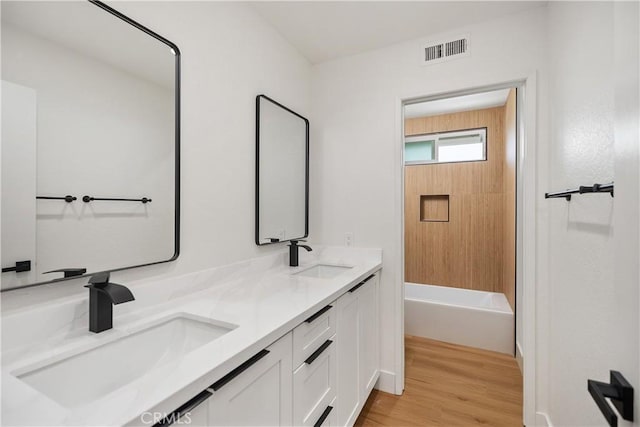 full bath with double vanity, visible vents, a sink, and wood finished floors