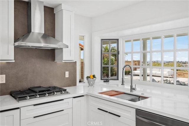 kitchen featuring a sink, white cabinetry, appliances with stainless steel finishes, wall chimney exhaust hood, and tasteful backsplash