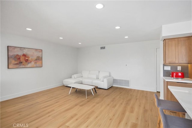 living area with light wood finished floors, visible vents, and baseboards