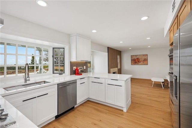 kitchen with stainless steel appliances, a peninsula, a sink, light countertops, and light wood-type flooring