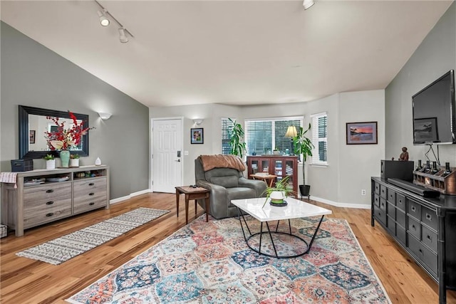 living room featuring lofted ceiling, light wood finished floors, track lighting, and baseboards