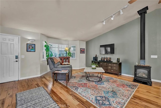 living area featuring light wood-style flooring, a wood stove, baseboards, vaulted ceiling, and rail lighting