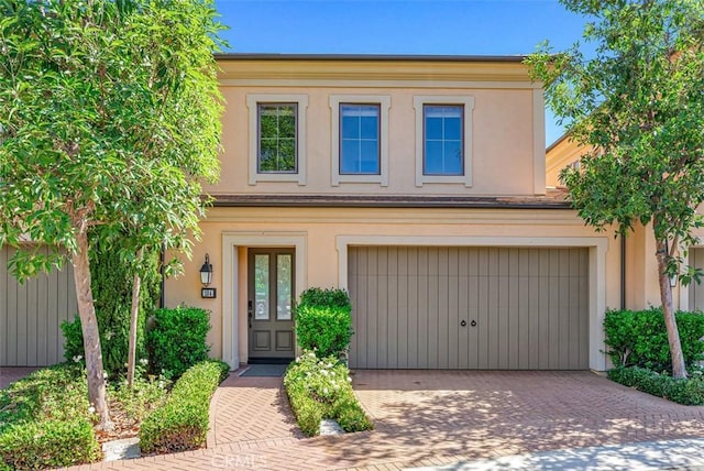 view of front of property featuring decorative driveway, an attached garage, and stucco siding