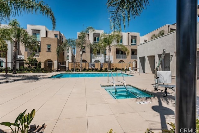 community pool with a residential view, a patio area, fence, and a hot tub