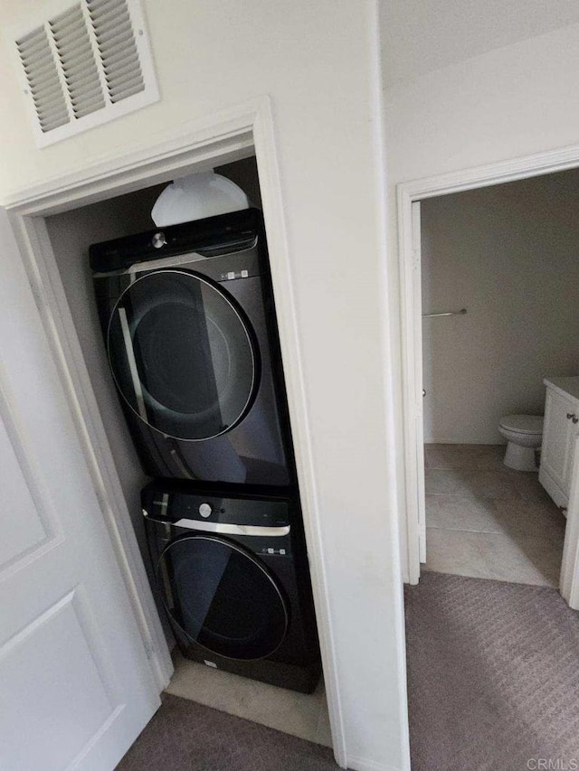 laundry room featuring carpet flooring, visible vents, and stacked washing maching and dryer