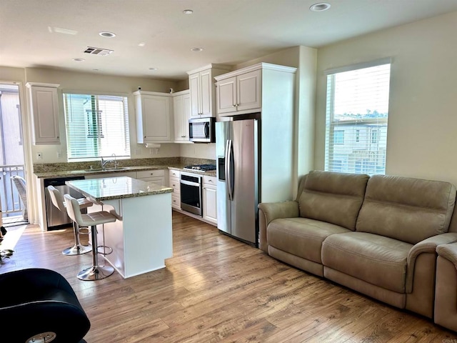 kitchen with open floor plan, white cabinetry, stainless steel appliances, and visible vents