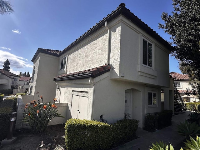 view of side of home with a tile roof and stucco siding