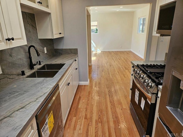 kitchen featuring light stone counters, stainless steel appliances, a sink, light wood-style floors, and backsplash