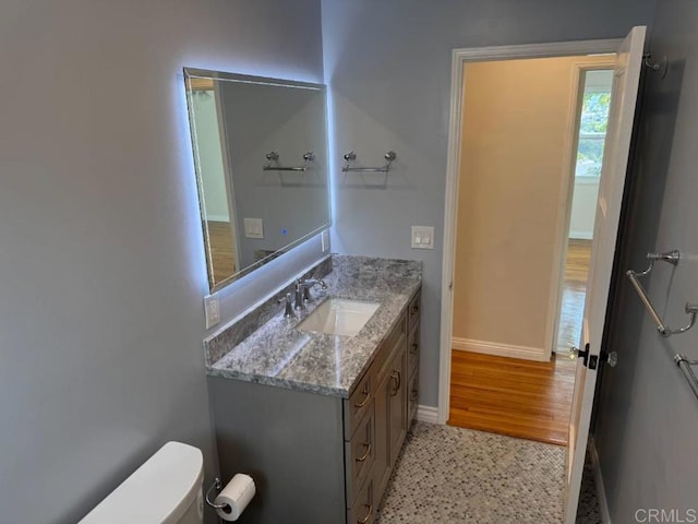 bathroom featuring speckled floor, baseboards, toilet, and vanity