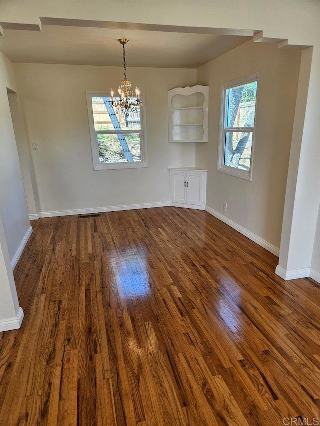 unfurnished dining area featuring a notable chandelier, baseboards, and dark wood-style flooring