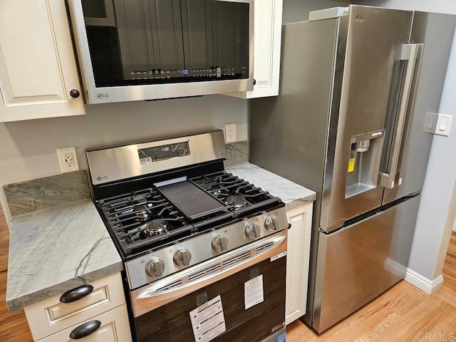 kitchen featuring baseboards, light stone countertops, light wood-style flooring, appliances with stainless steel finishes, and white cabinetry