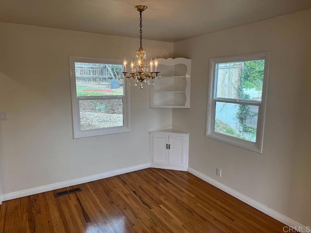 unfurnished dining area featuring visible vents, baseboards, a notable chandelier, and dark wood-style floors