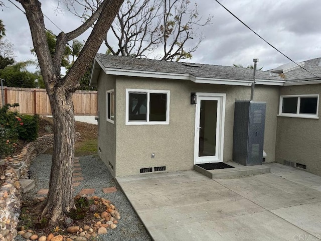 exterior space with a shingled roof, fence, stucco siding, crawl space, and a patio