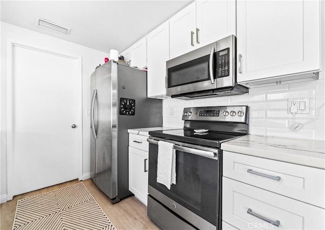 kitchen featuring tasteful backsplash, visible vents, white cabinets, light wood-style flooring, and appliances with stainless steel finishes