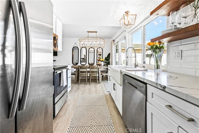 kitchen with light stone counters, stainless steel appliances, white cabinetry, open shelves, and a notable chandelier