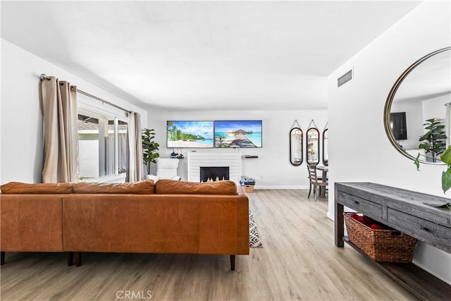 living room with light wood-style floors, a brick fireplace, visible vents, and baseboards