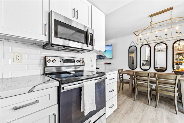 kitchen featuring tasteful backsplash, white cabinets, light stone counters, stainless steel appliances, and light wood-type flooring