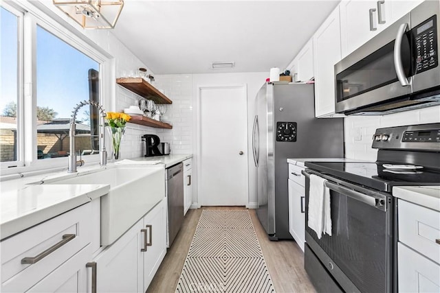 kitchen with light wood finished floors, visible vents, decorative backsplash, appliances with stainless steel finishes, and white cabinets