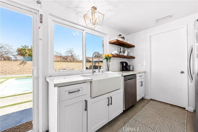 kitchen with visible vents, backsplash, stainless steel dishwasher, white cabinets, and a sink