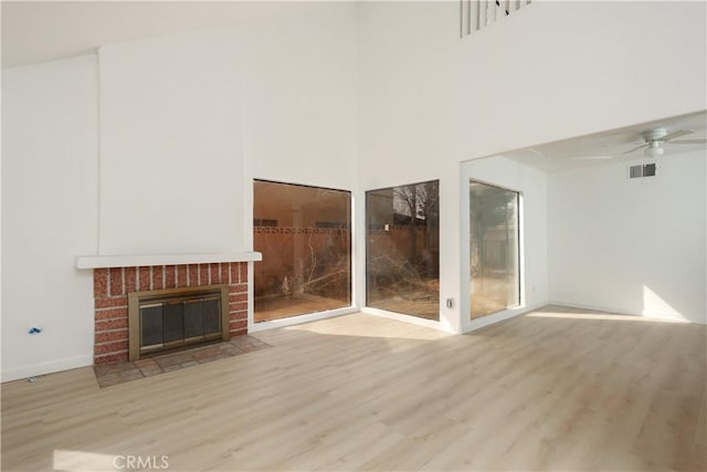 unfurnished living room with a brick fireplace, a ceiling fan, visible vents, and wood finished floors