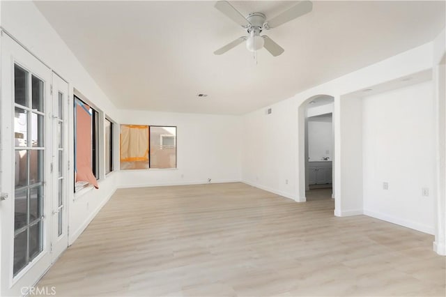 spare room featuring arched walkways, visible vents, light wood-style flooring, ceiling fan, and baseboards