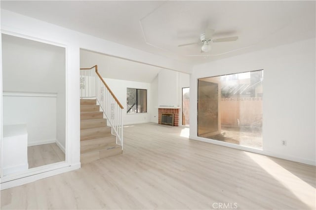 unfurnished living room with wood finished floors, a ceiling fan, vaulted ceiling, stairway, and a brick fireplace