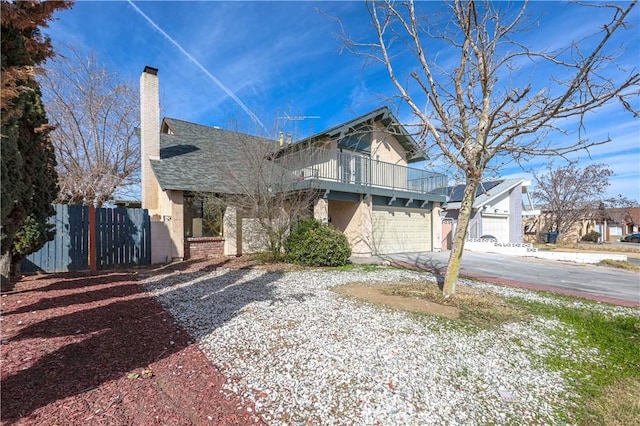 view of front of property featuring a chimney, fence, a balcony, a garage, and driveway