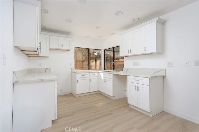 kitchen with baseboards, white cabinets, light stone counters, light wood-type flooring, and a sink