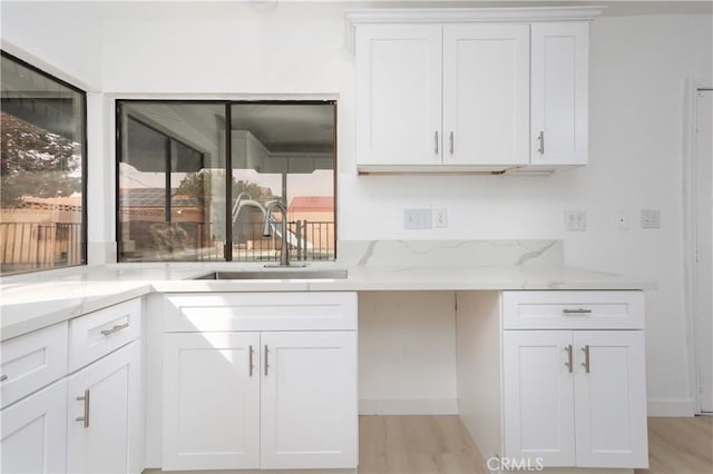 kitchen featuring light stone counters, light wood-type flooring, white cabinets, and a sink