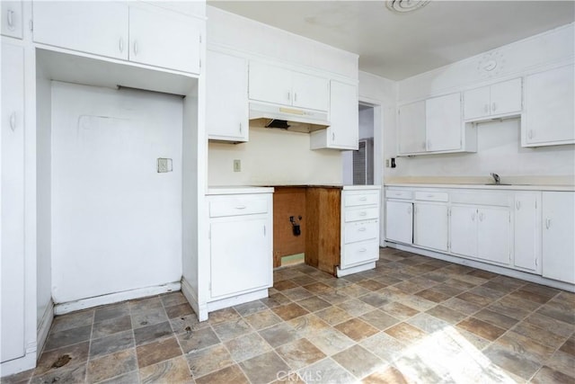 kitchen with under cabinet range hood, a sink, white cabinetry, light countertops, and stone finish flooring