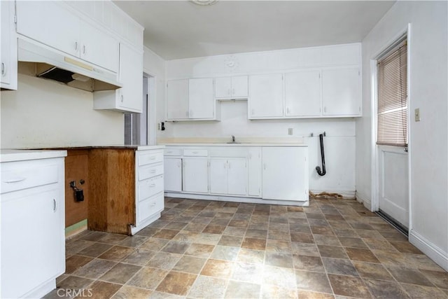 kitchen with baseboards, stone finish flooring, white cabinetry, and a sink